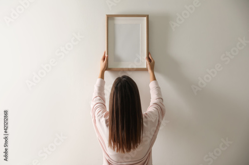 Woman hanging picture on white wall indoors photo