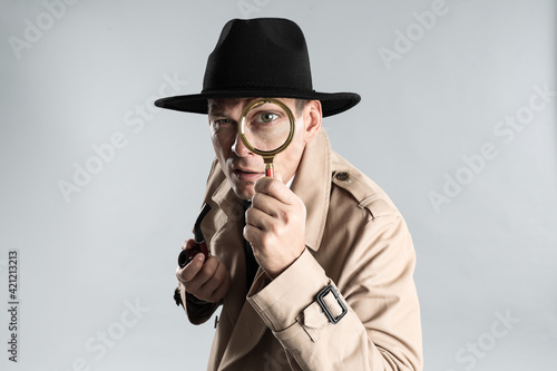 Male detective with smoking pipe looking through magnifying glass on grey background photo