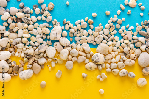 Sea light pebbles on a blue and yellow background, copy space, vacation on the sea or ocean, background like sand with water