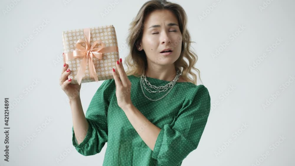 Slow motion of surprised young woman shaking decorated gift box and smiling feeling happy with present standing on white background alone. Celebrations and people concept. Slow motion of surprised young woman shaking decorated gift box and smiling feeling happy with present standing on white background alone. Celebrations and people concept.