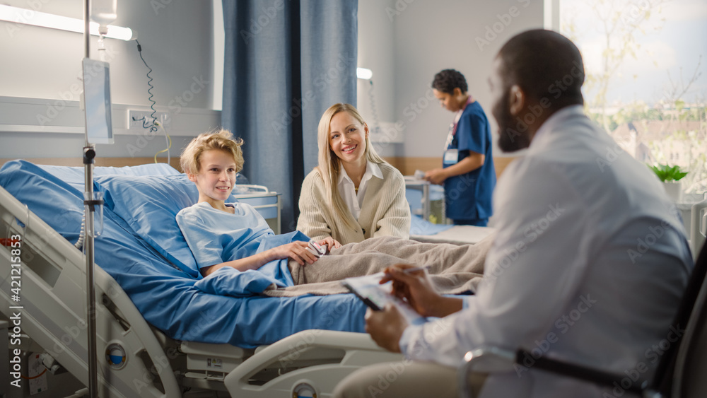 Hospital Ward: Handsome Young Boy Resting in Bed with Caring Mother Visits to Support Him, Friendly Doctor Talks, Gives Advice, Explains Test Results. Happy Smiling Patient Recovering after Sickness Hospital Ward: Handsome Young Boy Resting in Bed with Caring Mother Visits to Support Him, Friendly Doctor Talks, Gives Advice, Explains Test Results. Happy Smiling Patient Recovering after Sickness