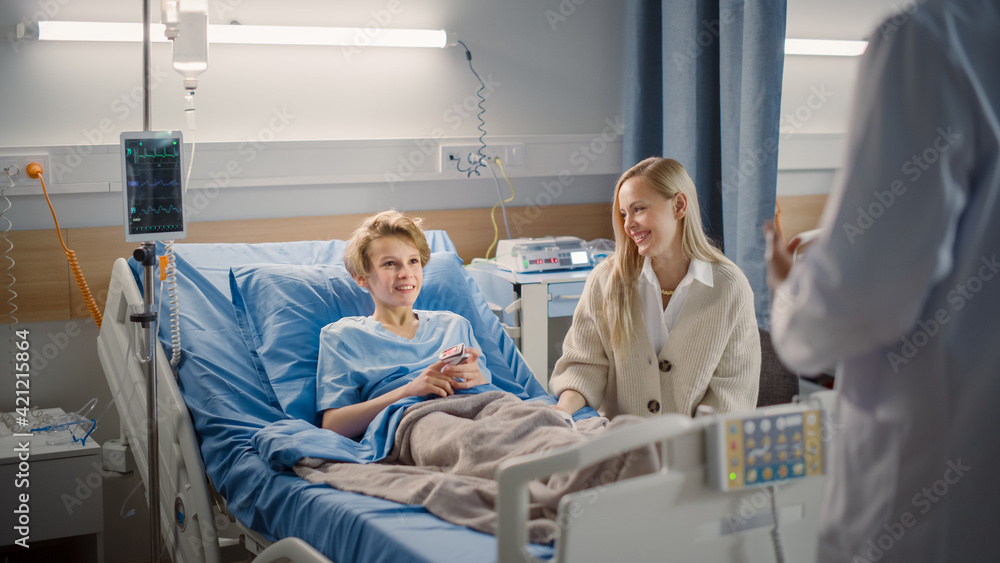 Hospital Ward: Handsome Young Boy Resting in Bed with Caring Mother Visits to Support Him, Friendly Doctor Talks, Gives Advice, Explains Test Results. Happy Smiling Patient Recovering after Sickness Hospital Ward: Handsome Young Boy Resting in Bed with Caring Mother Visits to Support Him, Friendly Doctor Talks, Gives Advice, Explains Test Results. Happy Smiling Patient Recovering after Sickness