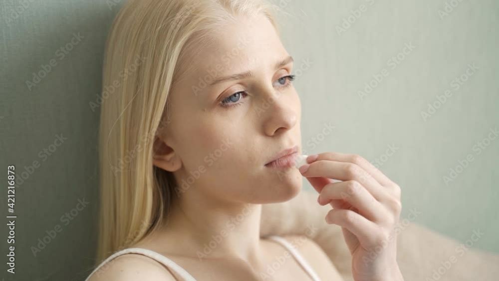 Sick woman taking pills holding a glass of water sitting on a sofa at home. Sick woman taking pills holding a glass of water sitting on a sofa at home.