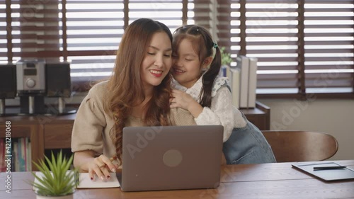 Asian mother working from home laptop computer on table his daughter giving shoulder massage to mother for stress relief, Medium panning shot of smiling mother and daughter using laptop 