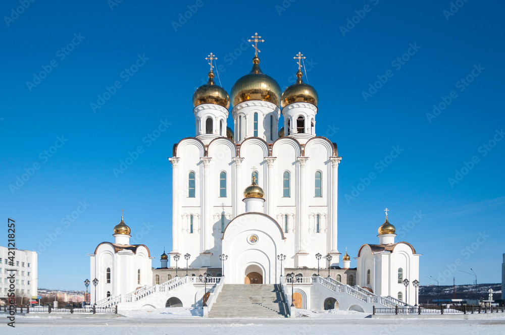 Trinity christian orthodox cathedral in Magadan, Russia, white church with golden domes on sunny winter day with clear blue sky