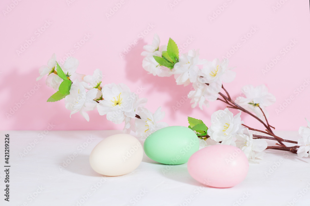 Easter eggs, pink, beige and green, on a concrete white table, next to flowers on a pink background. Pastel shades. Copy space