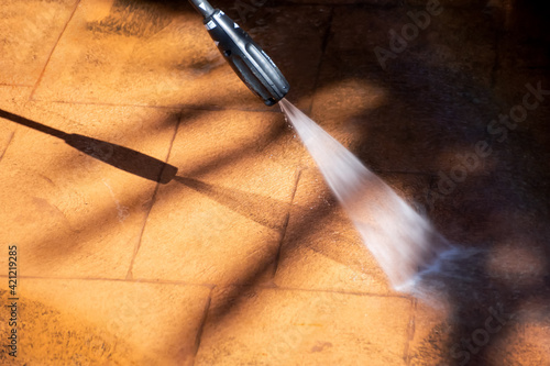 Cleaning backyard paving tiles with pressure washer cleaner.