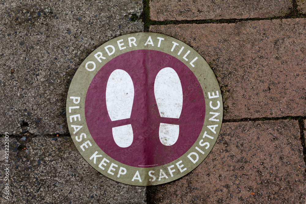 Floor foot print sign at a coffee shop or restaurant asking to asking at till and keep a safe distance from other customers