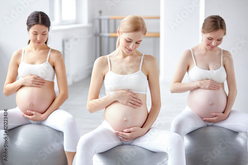 cute diverse pregnant women with naked tummy sit on fitballs engaged in perinatal gymnastics