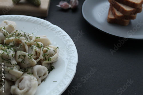 Folk traditional cuisine dishes dumplings sprinkled with fennel greens served with garlic bread in a white festive plate on a black dark background with a place for the text of the copyspace