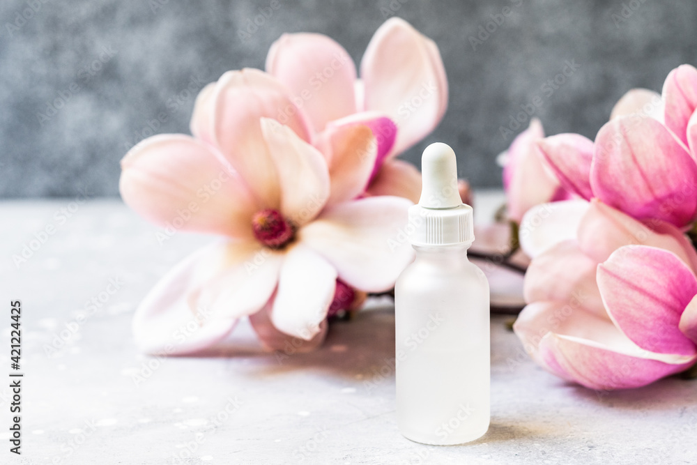 Serum with floral magnolia extracts for skincare. Nature cosmetics in glass bottle with a pipette and with flowers on grey background. Organic Spa Cosmetic With floral Ingredients. Serum with floral magnolia extracts for skincare. Nature cosmetics in glass bottle with a pipette and with flowers on grey background. Organic Spa Cosmetic With floral Ingredients.