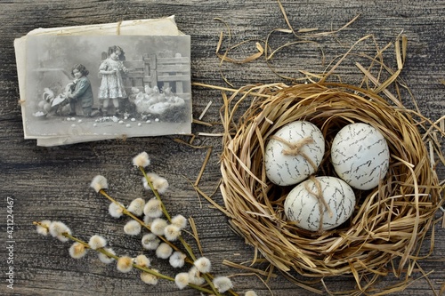 Easter decorative composition in vintage style with retro greeting postcard, decoupaged Easter eggs  in a nest on old wooden background with willow twigs top view.