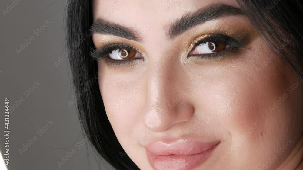 Very beautiful young woman model posing in photo studio. Portrait of a girl with a bright evening smoky eye make-up, dark hair and brown eyes looks at camera close up view Very beautiful young woman model posing in photo studio. Portrait of a girl with a bright evening smoky eye make-up, dark hair and brown eyes looks at camera close up view