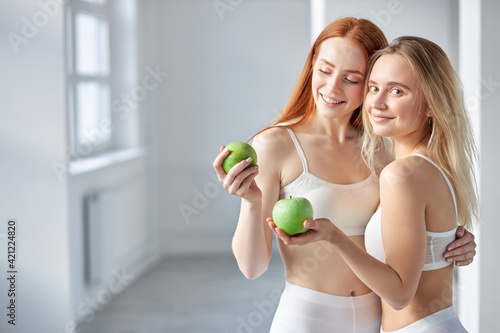 Two Athlete Women With Blonde And Red Hair Posing With Green Apples