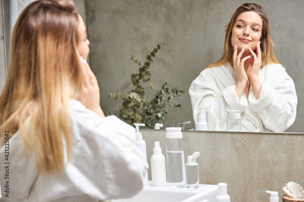 Young and beautiful. Female looking at bathroom mirror after taking shower, enjoying clean healthy skin Young and beautiful. Female looking at bathroom mirror after taking shower, enjoying clean healthy skin