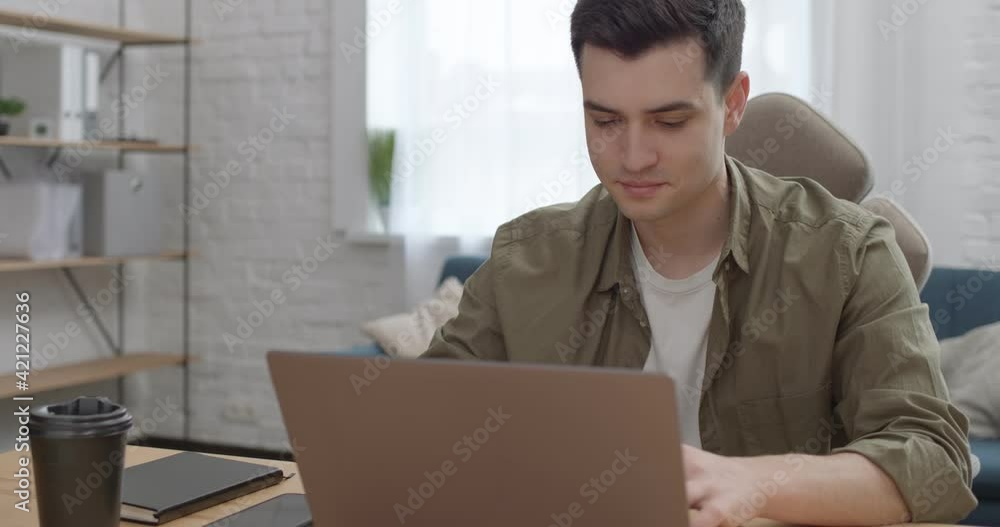 Attractive Young Businessman Typing Message looking on Laptop Screen. Successful Entrepreneur sitting at comfortable Office Room using Computer for Distance Work. Surfing. Device. Busy People. Attractive Young Businessman Typing Message looking on Laptop Screen. Successful Entrepreneur sitting at comfortable Office Room using Computer for Distance Work. Surfing. Device. Busy People.