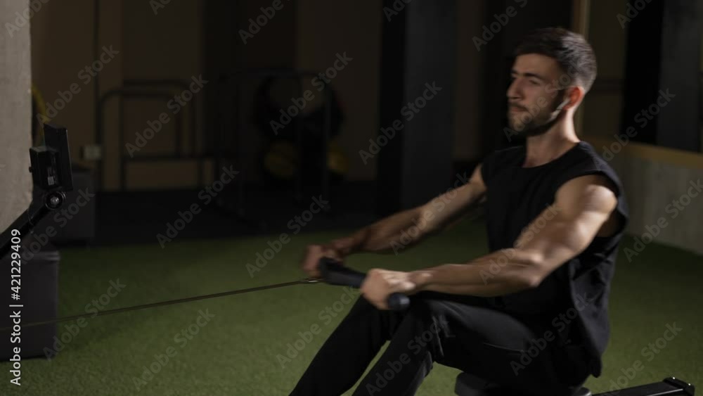 Bearded sportsman works out in gym with rowing machine Bearded sportsman works out in gym with rowing machine