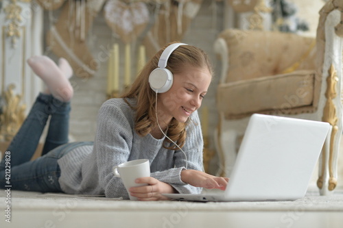 Girl in headphones using laptop while lying on floor