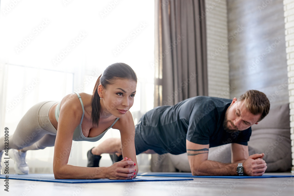 Good-looking Slim Couple Performing Plank At Home In Living Room Good-looking Slim Couple Performing Plank At Home In Living Room