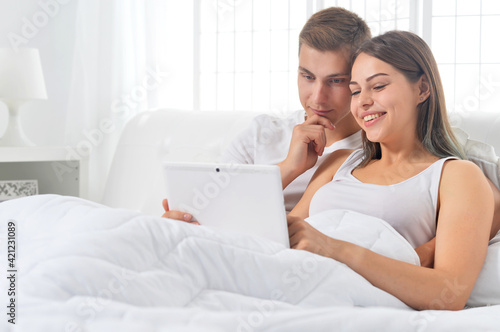 Beautiful young couple on soft bed in  morning with laptop
