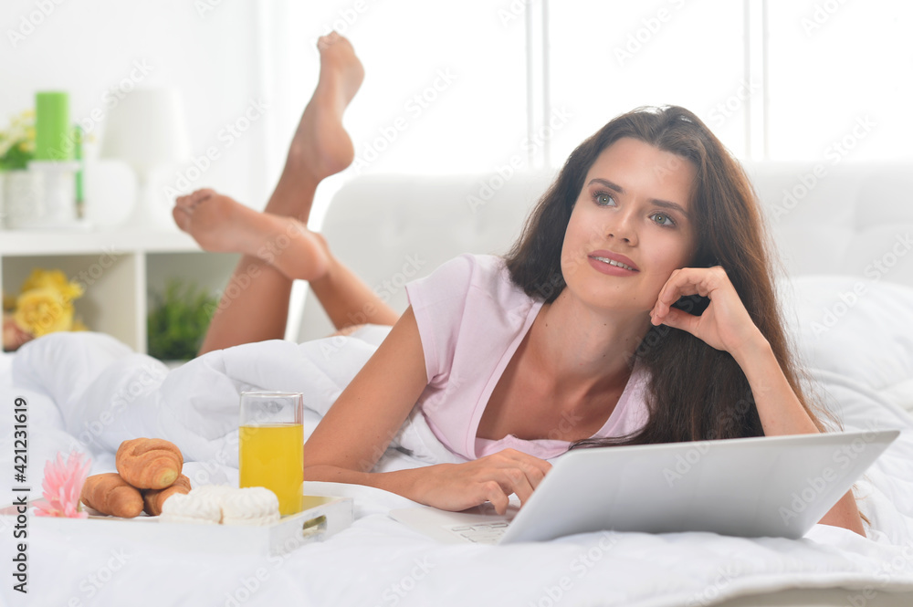 Young beautiful woman having breakfast and using laptop in bed Young beautiful woman having breakfast and using laptop in bed
