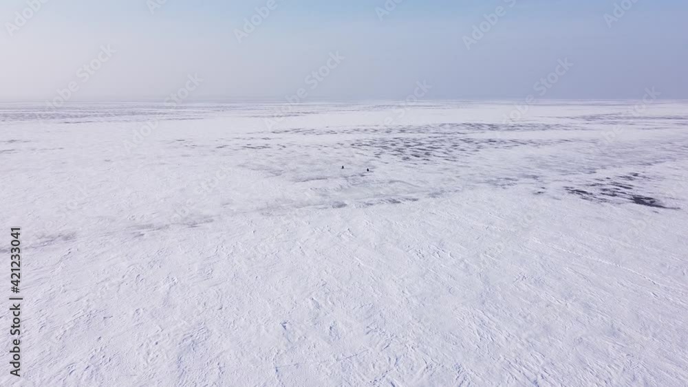 Aerial drone flight above two winter fishers sitting in the middle of an icy desert Aerial drone flight above two winter fishers sitting in the middle of an icy desert