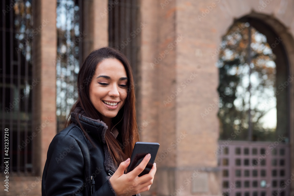 Fototapeta premium smiling woman looking at her phone at the street