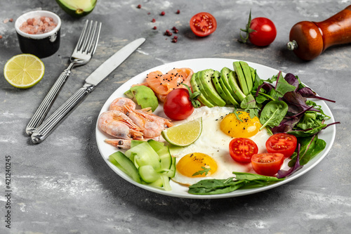 Ketogenic breakfast. Keto low carb salmon, boiled shrimps, prawns, fried eggs, fresh salad, tomatoes, cucumbers and avocado. Top view
