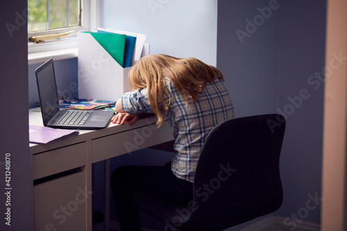 Bored Girl Sitting Lying Head On Desk Whilst Home-Schooling With Laptop During Health Pandemic