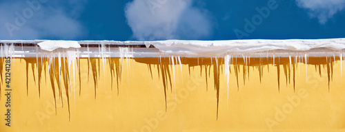 Row of sharp icicles on snowy roof. Risk of icicles falling off the roof. Dangerous icicles hang down the rooftop