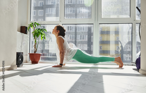 Side view of a young woman practicing Urdhva Mukha Svanasana yoga pose at home. photo