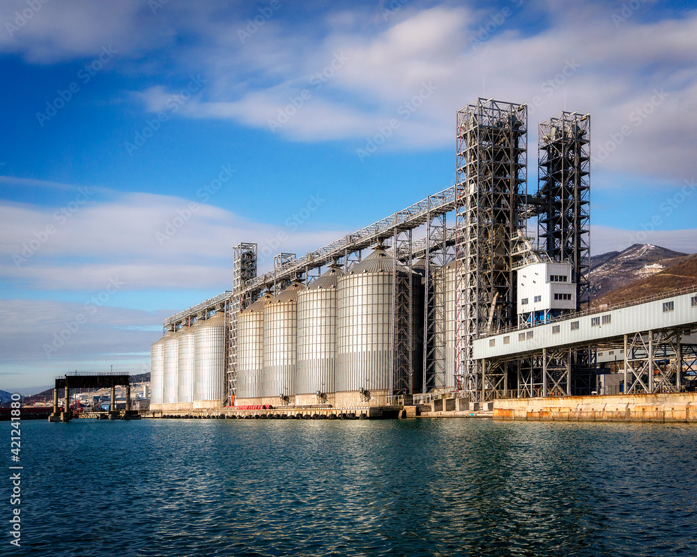 Grain storage tanks in the port next to the sea with a blue sky
