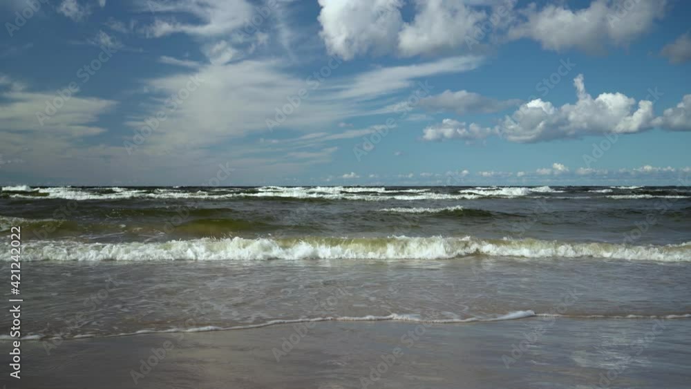 Waves run into a storm on a sandy Baltic beach in Latvia. Beautiful clouds over the horizon against the blue sky. Waves run into a storm on a sandy Baltic beach in Latvia. Beautiful clouds over the horizon against the blue sky.