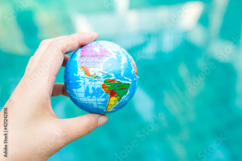Earth day concept, plastic global ball in girl hand over blurred blue water background, outdoor day light, international earth day concept