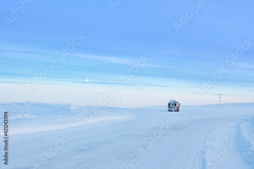 Red truck  covered with snow  driving on the snowy road in tundra. Morning arctic simple winter landscape in Murmansk region of Russia