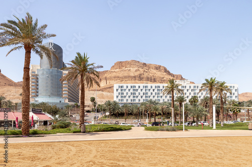 View of the beach on the Ein Bokek embankment on the coast of the Dead Sea  tourist hotels and sandy mountains in the background  in Israel