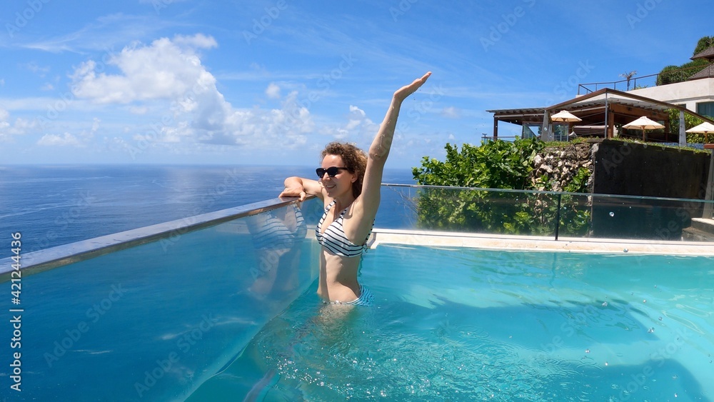 Caucasian girl in an infinity swimming pool. Camera showing the ocean underneath