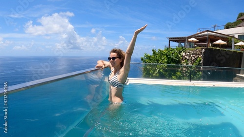 Caucasian girl in an infinity swimming pool. Camera showing the ocean underneath