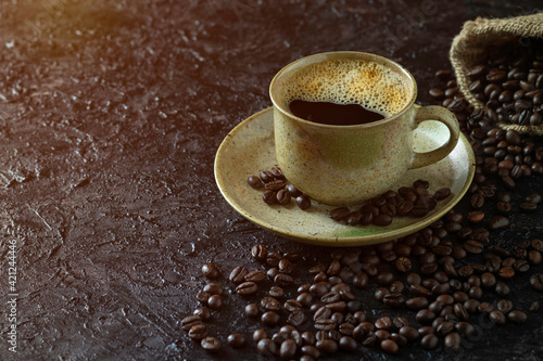 Hot black coffee for morning beverage menu in vintage brown ceramic cup with coffee beans roasted in burlap sack bag on dark grunge rustic table background. Flat lay with copy space.