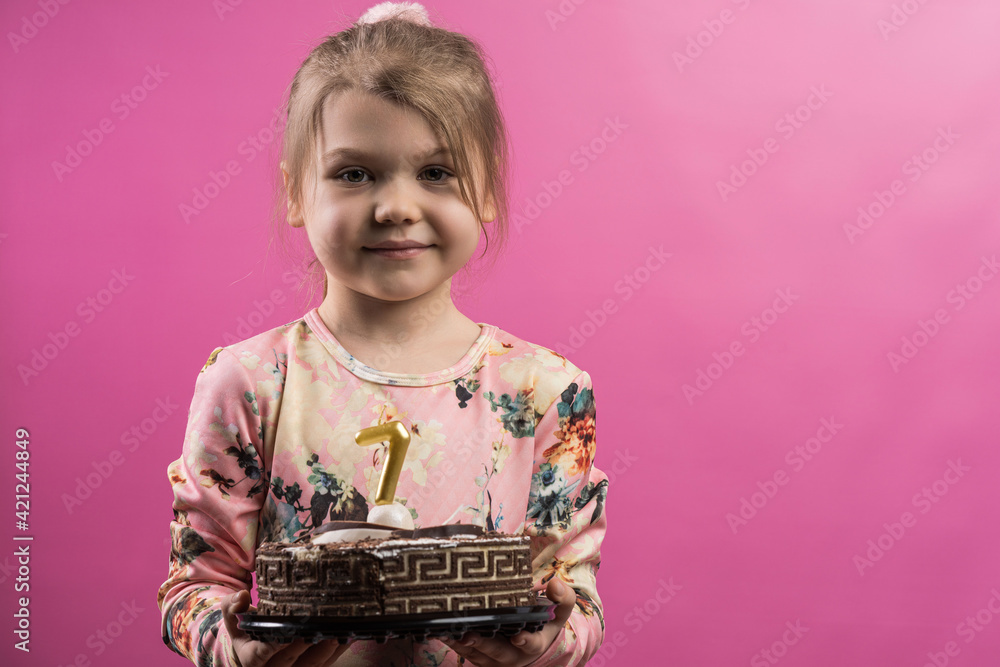 The girl is celebrating her birthday. child blows out the candle on the cake on a pink background and celebrates seven years.
