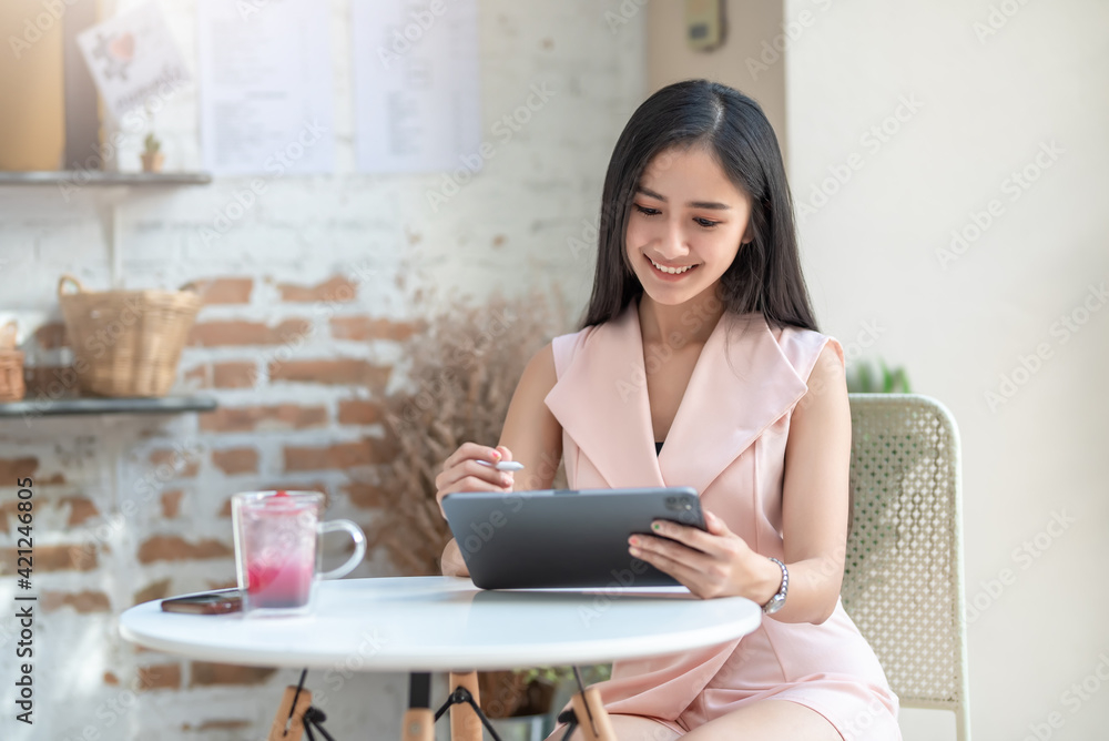 Image of a charming Asian woman sitting at a coffee shop using a tablet. Image of a charming Asian woman sitting at a coffee shop using a tablet.