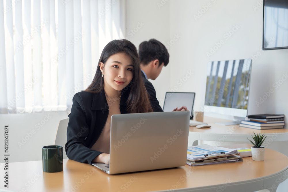 Young Asian businesswoman working using laptop at the office. Looking at the camera. Young Asian businesswoman working using laptop at the office. Looking at the camera.