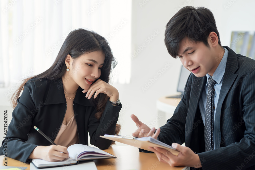 Two young Asian business people explaining a list of collaboration using document and taking notes at the office. Two young Asian business people explaining a list of collaboration using document and taking notes at the office.