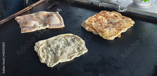 Roti canai or paratha bread being fried on flat pan