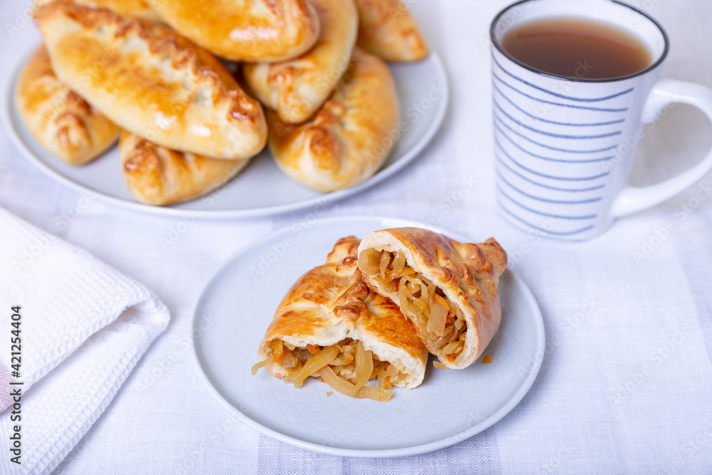 Pies (pirozhki) with cabbage. Homemade baking. Traditional Russian and Ukrainian cuisine. In the background is a dish with pies. Close-up. Pies (pirozhki) with cabbage. Homemade baking. Traditional Russian and Ukrainian cuisine. In the background is a dish with pies. Close-up.