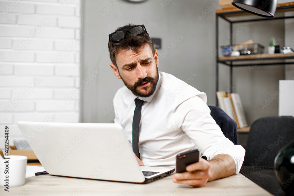 Handsome businessman using the phone in the office.  Young manager typing a message