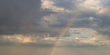 rainbow on dramatic dark sky with rays and white clouds