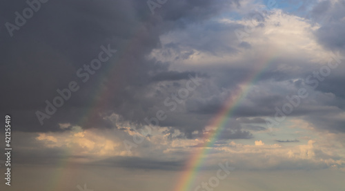 rainbow on dramatic dark sky with rays and white clouds