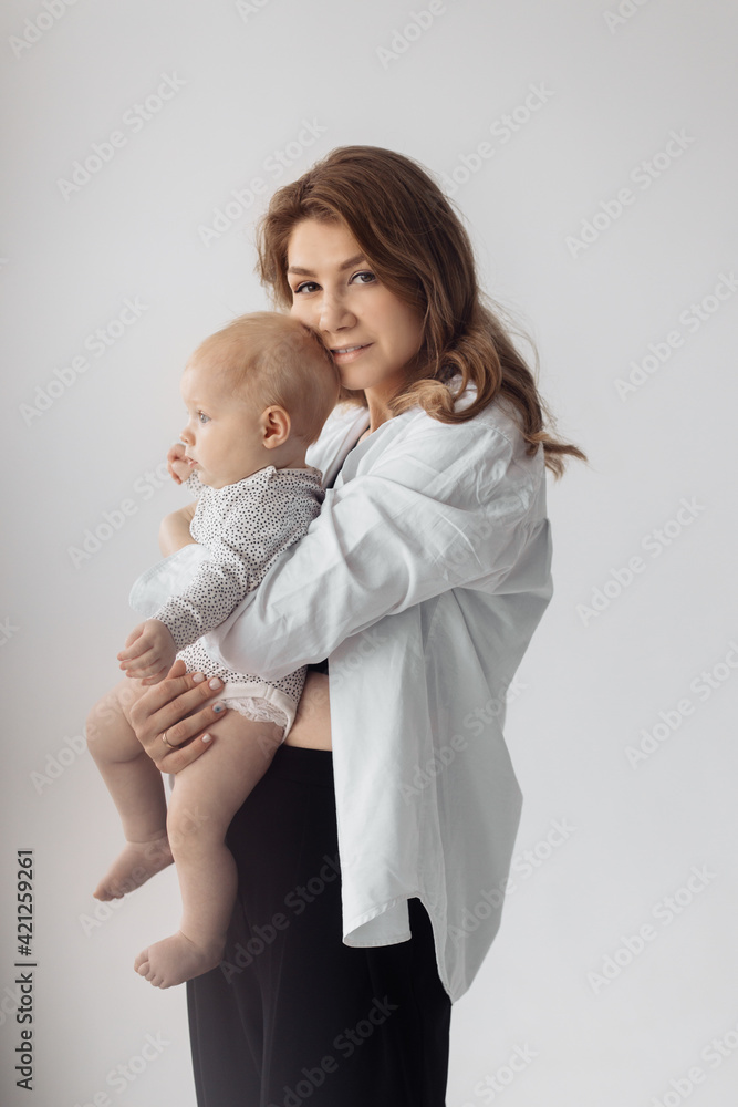 Portrait of beautiful stylish woman with a cute child in the studio. Gorgeous young mother with lovely daughter in her arms is looking at the camera, smiling Portrait of beautiful stylish woman with a cute child in the studio. Gorgeous young mother with lovely daughter in her arms is looking at the camera, smiling