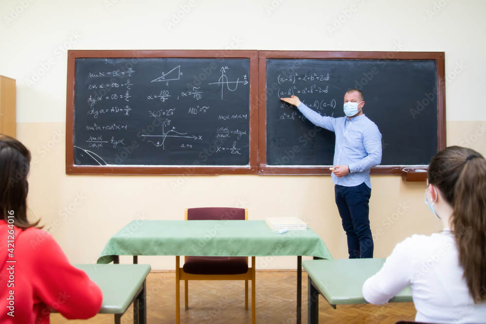 Students in protective face masks studying in classroom with teacher. Precautions in coronavirus pandemic Students in protective face masks studying in classroom with teacher. Precautions in coronavirus pandemic